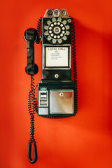 Black vintage metal Public telephone with a coin box on a red wall. Vintage things.