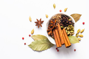 Wall Mural - Exotic herbal Food concept Mix of the organic Spices cinnamon stick, cardamom pods, bay leaves, star anise and coriander seedsin white ceramic cup on white background