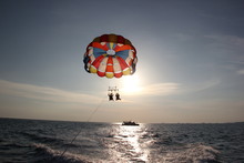 A Young Man And A Girl Are Flying On A Double Parachute Behind A Boat Over The Sea.
