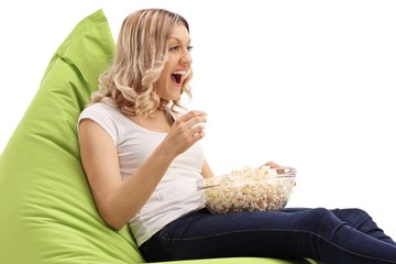 Sticker - Joyful young woman sitting on a beanbag and eating popcorn