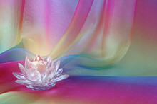 Lotus Light Rainbow Chiffon Background - A Lotus Flower Shaped Cut Glass Candle Holder With A Lit Candle, Against Rainbow Coloured Draped Flowing Chiffon Material
