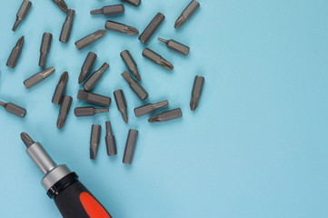 One screwdriver with rubber handle of black and orange color and scattered metal bits on blue background with copy space