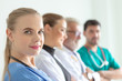 © thbangkok - Confident female doctor looking at camera and smiling while her colleagues standing in a row behind her. A team of experienced highly qualified doctors.