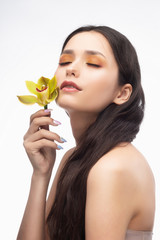 Wall Mural - A beautiful brunette nude shoulders girl sensually holds a flower of an orchid in her hands. Nude make-up. Healthy smooth skin