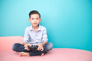 Young boy isolated in blue. Handsome early teenage boy portrait. Playing game console with joy pad. Technology concept.