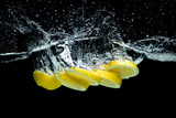 Fototapeta  - close up view of fresh lemon pieces in water with splashes isolated on black