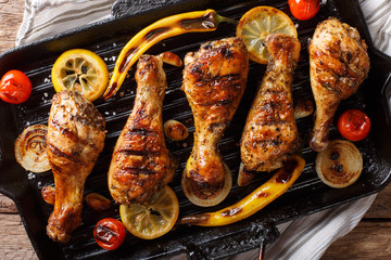 Canvas Print - Delicious food: grilled chicken drumstick legs with vegetables in a grill pan close-up on a table. horizontal top view, rustic