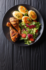 Delicious food: grilled chicken drumsticks with new potatoes and fresh salad closeup on a plate. Vertical top view