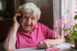Elderly woman talks on a mobile phone sitting at home.