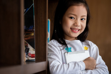 cute girl smile standing and holding tablet smartphone in the library, children concept, education concept