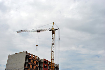 Mounting crane at construction of apartment building, cloudy sky background