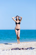 © azazello - Attractive young woman in bikini walking on pebble beach