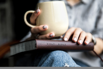 Wall Mural - Young woman reading a book and holding cup of tea or coffee.