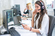 © Bojan - Smiling young woman with headset using phone in office