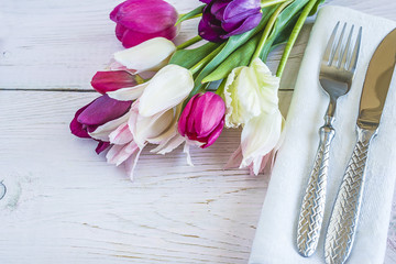 Wall Mural - Festive table setting with beautiful cutlery on a white linen napkin and bouquet of multicolored tulips on white wooden background wiith copy space