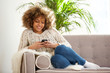 © mimagephotos - young african woman relaxing at home and using mobile phone