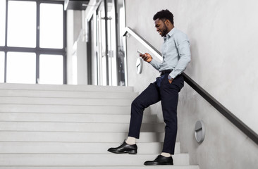 Canvas Print - business, people and technology concept - african american businessman with smartphone at office stairs