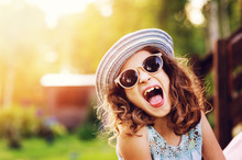 Summer Portrait Of Happy Kid Girl On Vacation In Sunglasses And Hat, Laugh And Showing Tongue.