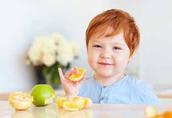 Wall Mural - cute redhead toddler baby tasting orange slices and apples at the kitchen