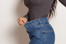Latin Woman In Baggy Pants, Indoors, Over A White Wall. Weight Loss Concept.