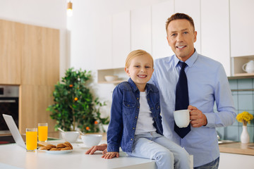 Wall Mural - Happy family. Happy girl sitting on the table and keeping smile on face while spending time with daddy