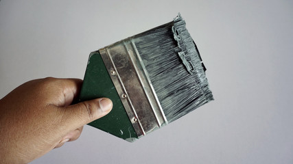 A hand holding a Brush painting which has been used with green wood handle on white background