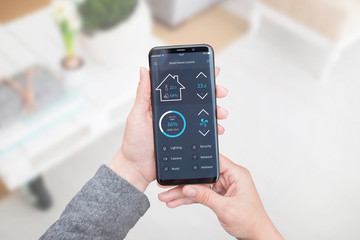 Smart home control app for mobile devices in woman hand. Living room interior in background.