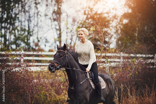 Fotografía Young woman riding her horse through a pasture in autumn