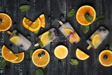 Homemade detox popsicles with blueberries, orange slices and mint leaves on black wood