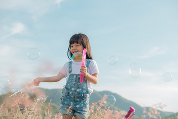 Adorable little girl, has happy fun with cheerful smiling face. Carefree child Running and jumping on green summer meadow, catching soap bubbles. Happiness, childhood and freedom concept.