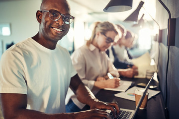 smiling african designer working on a laptop with his team