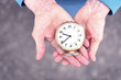 Elderly woman holds an alarm clock in wrinkled hands. Hands of elderly grandmother. Concept of time is not standing still.