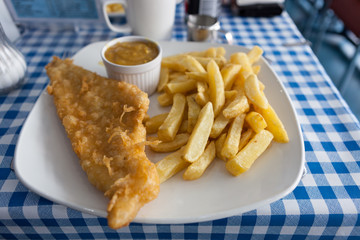 Authentic British fish and chips, with curry sauce, on a blue and white chequered table cloth.