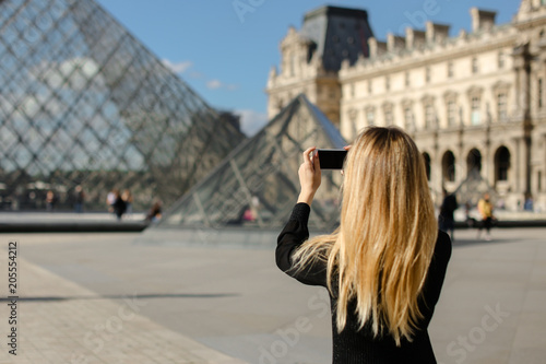 Girl standing near Louvre and glass pyramind in black dress in Paris, talking photo by smartphone Poster Mural XXL