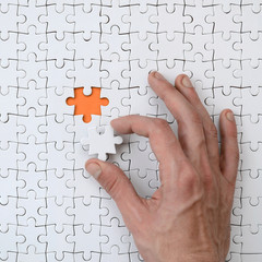 Wall Mural - The texture of a white jigsaw puzzle in the assembled state with one missing element that the male hand puts in