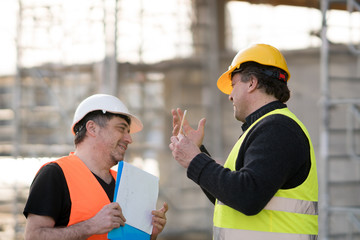 Two happy civil engineers wearing protective vests and helmets at work on construction site