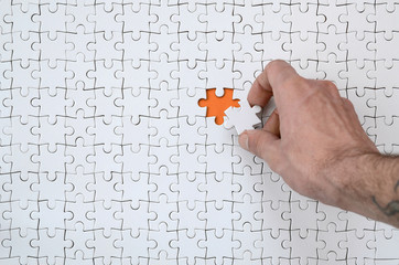 Wall Mural - The texture of a white jigsaw puzzle in the assembled state with one missing element that the male hand puts in