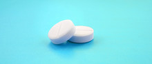 A Few White Tablets Lie On A Bright Blue Background Surface. Background Image On Medical And Pharmaceutical Topics
