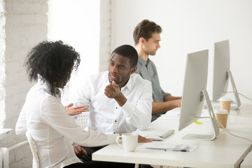 Wall Mural - Serious african colleagues discussing project together at workplace, black coworkers talking solving business problem in multiracial office, afro american teammates having disagreement or conflict at