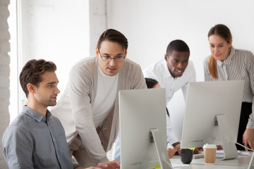 Corporate mentor teaching intern helping and supervising online computer work, team leader or company executive explaining new web design project or programming task to employee at workplace