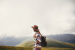 travel and wanderlust concept. traveler hipster girl in hat with backpack exploring misty sunny mountains in clouds. space for text. stylish woman traveling. amazing atmospheric moment.