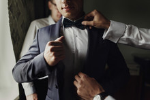 Stylish Groomsmen Helping Happy Groom Getting Ready In The Morning For Wedding Ceremony. Luxury Man In Suit In Room. Space For Text. Wedding Day.