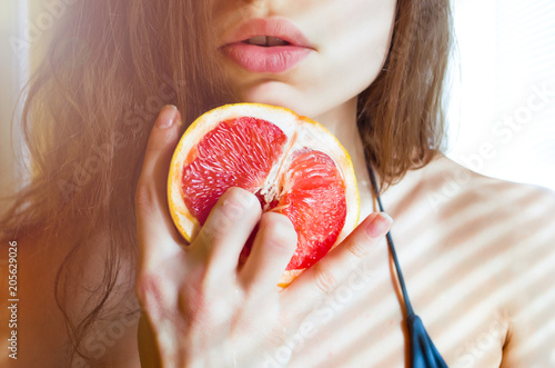 Fotografie, Obraz beautiful young sexy woman in bikini holding two fingers on grapefruit on the background of her lips