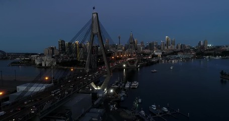 Poster - Cables holding wide stretches of Anzac bridge in Sydney over harbour waters at sunset in view of illuminated city CBD towers.
