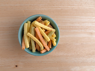 Top view of veggie straws in a green bowl on a wood table.