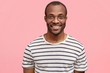 © wayhome.studio  - Handsome delighted guy with dark skin, pleasant smile, wears casual striped t shirt, poses against pink background, expresses positive emotions and feelings. People, facial expressions concept