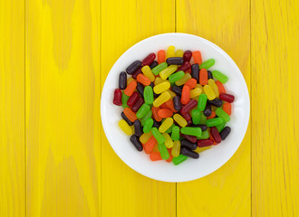 Wall Mural - Chewy colorful candy on a white plate atop a bright yellow table.