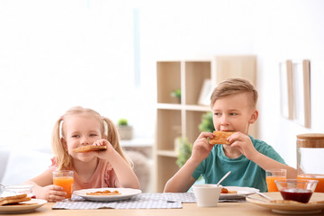 Adorable little children eating tasty toasted bread with jam at table