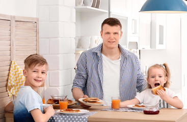 Wall Mural - Father and cute little children having breakfast with tasty toasted bread at table