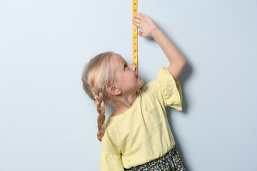 Wall Mural - Little girl measuring her height on light background